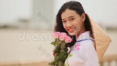 <strong>越南</strong>女孩穿着<strong>民族</strong>服装和服装，为相机摆姿势和微笑。 手里拿着粉红色